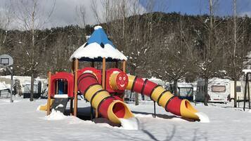 Une aire de jeux recouverte de neige, avec un toboggan et une structure d’escalade.