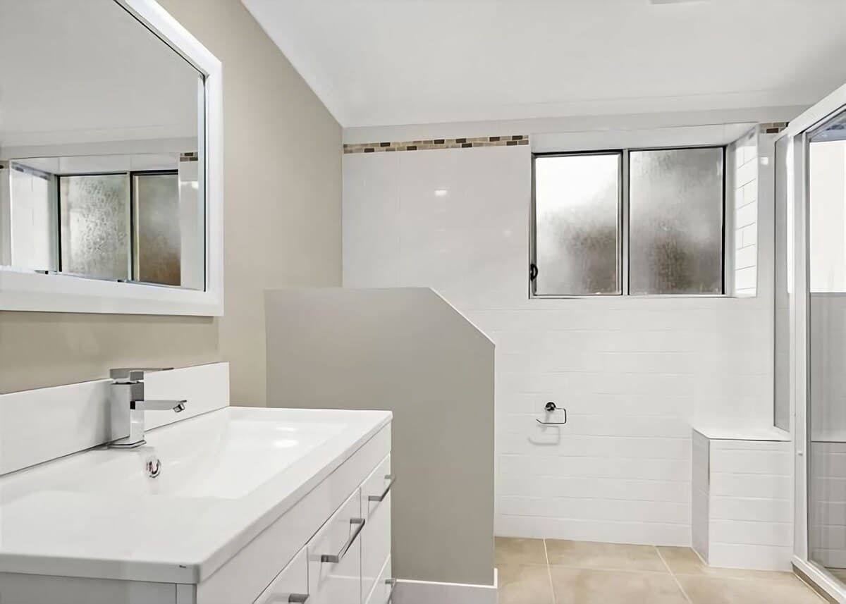 Un baño moderno con un espejo grande, tocador blanco y zona de ducha.