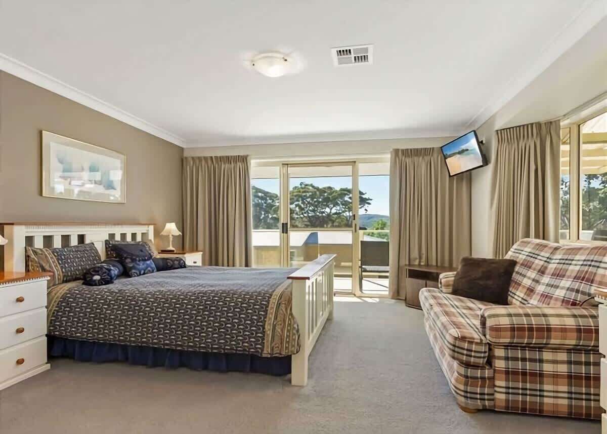 Een slaapkamer met een bed, een slaapbank, een televisie en een balkon met gordijnen.