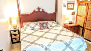Un lit bien fait, recouvert d’une couvre-lit à motifs, agrémenté d’un coussin décoratif et flanqué de deux tables de chevet dotées de lampes et de tiroirs de rangement.