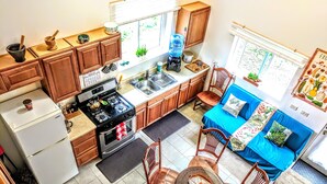 Une cuisine compacte équipée d’une cuisinière, d’un évier et d’un réfrigérateur. On y trouve une table à manger avec des chaises, ainsi qu’un canapé bleu agrémenté de coussins.