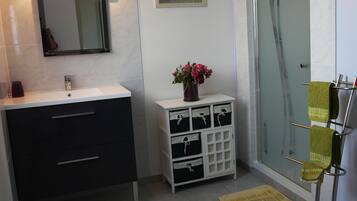 A bathroom with a white sink, dark cabinets, a mirror, a vase with flowers, a glass shower enclosure, and a towel rack.