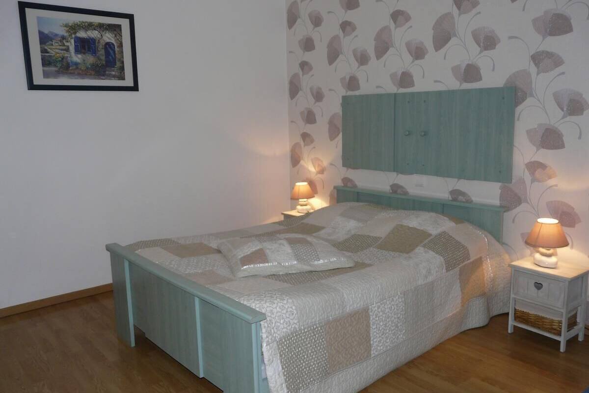 A bedroom with a bed, two bedside tables, a nightstand, a wall-mounted headboard, and a framed picture on the wall.