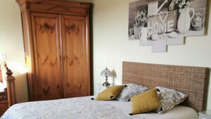 A bedroom with a large bed, a wooden wardrobe, and a wall-mounted artwork. - Chambres d'hôtes le Pot au Lait (Villaines-la-Juhel)