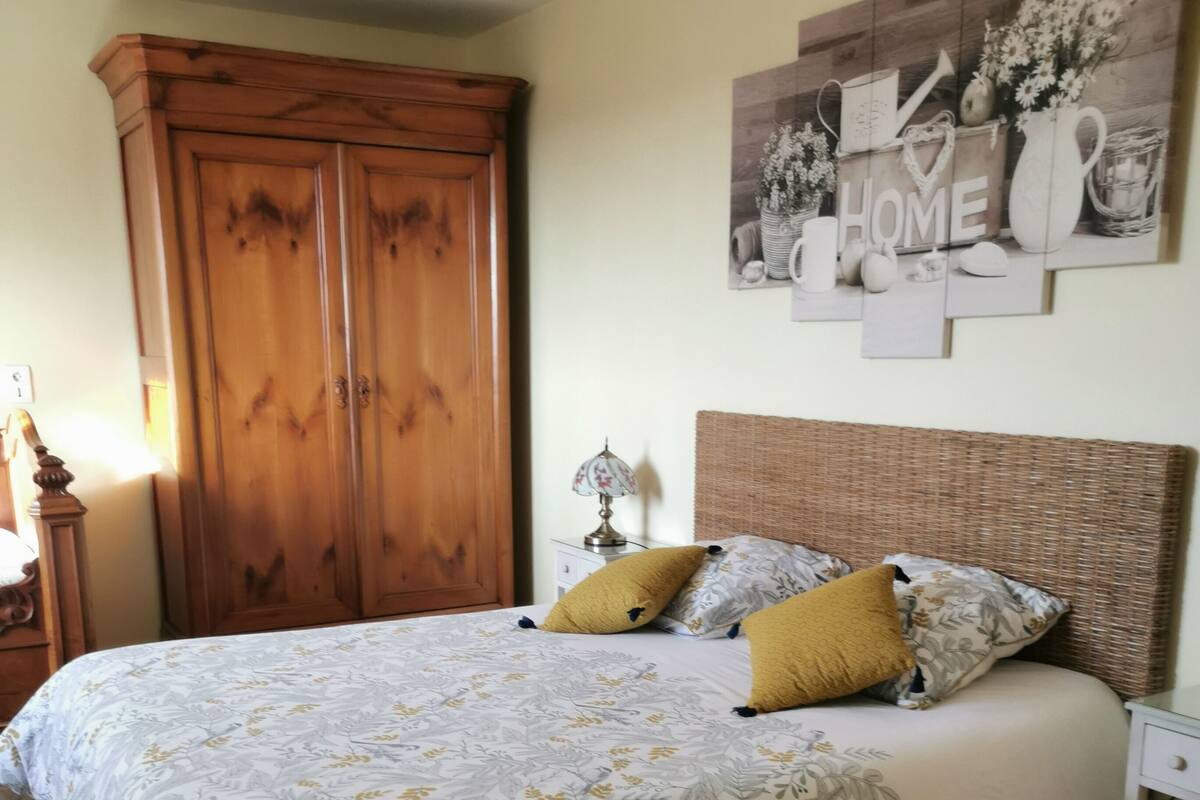 A bedroom with a large bed, a wooden wardrobe, and a wall-mounted artwork.