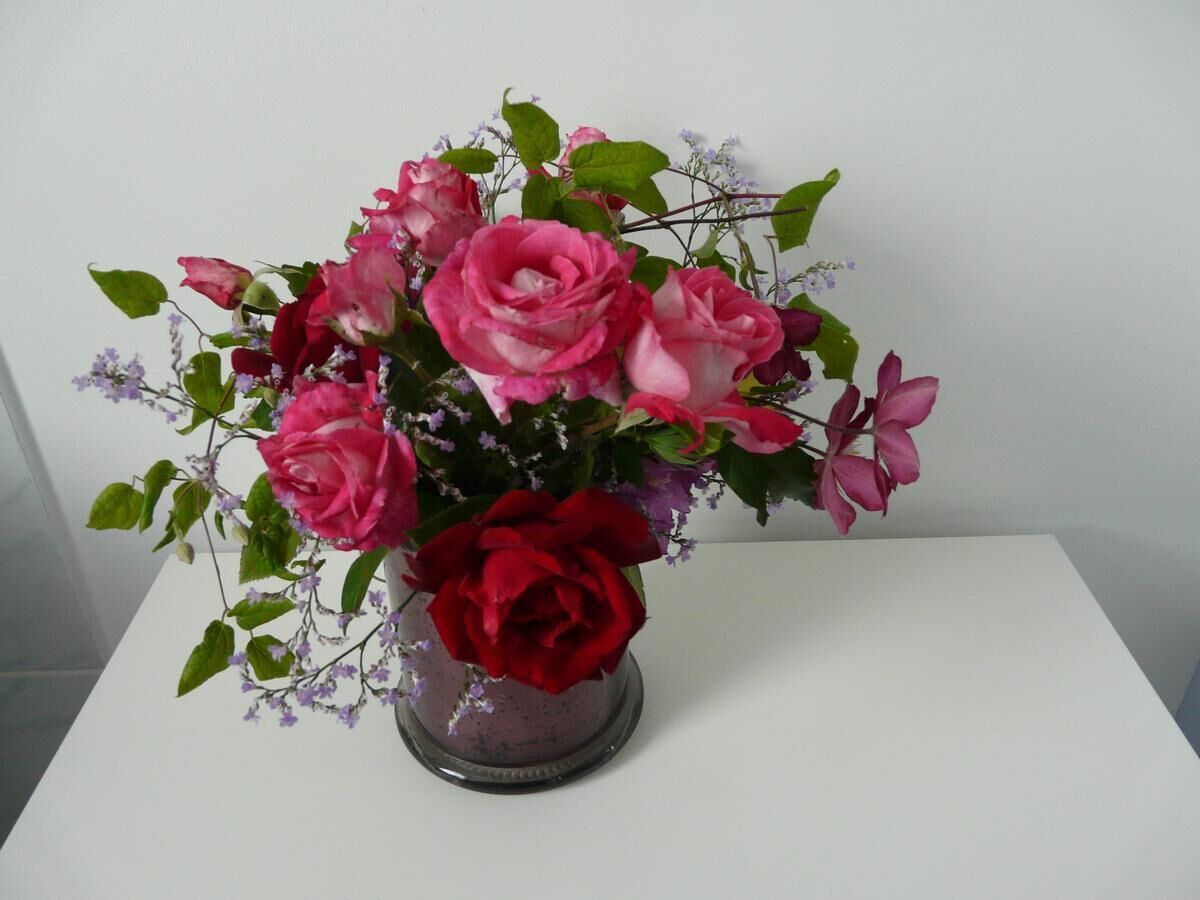 A bouquet of pink and red roses in a clear glass vase on a white table.