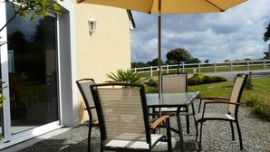 An outdoor patio with a table and chairs, a yellow umbrella, and a gravel ground. - Chambres d'hôtes le Pot au Lait (Villaines-la-Juhel)