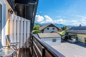 A balcony with a table and chairs, a view of a parking area, and houses in the background. - Rooms & Apartments Jana (Cerklje na Gorenjskem)