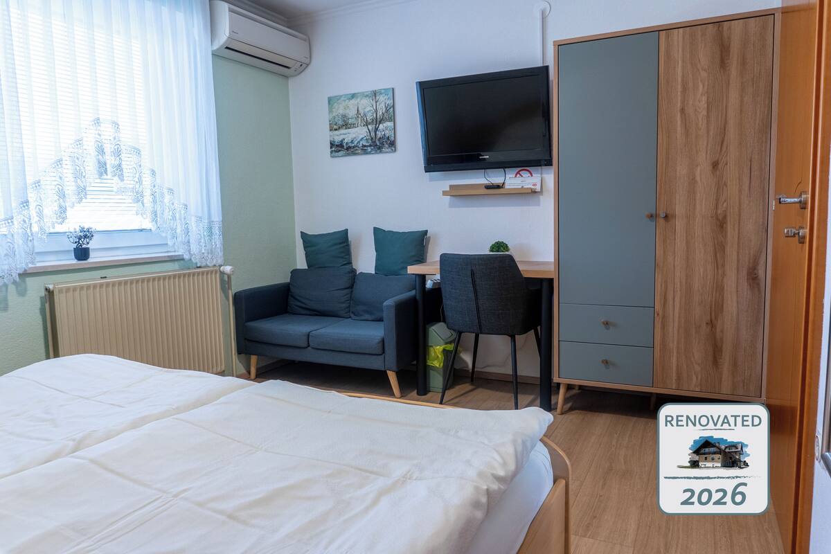Ein Schlafzimmer mit einem Bett, einem Schreibtisch, einem Sessel, einem Fernseher und einem Kleiderschrank.