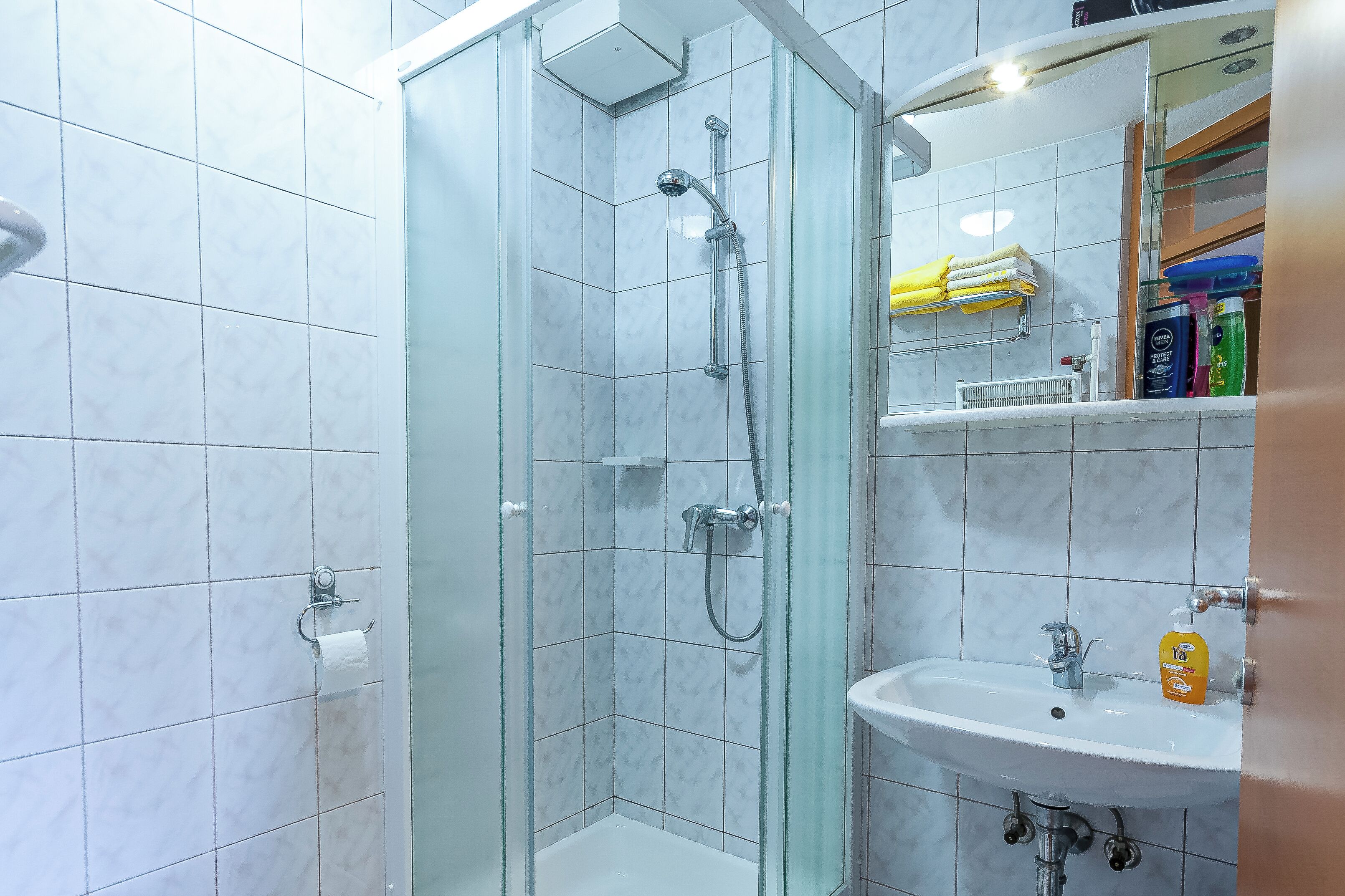 A bathroom with a glass-enclosed shower, a sink, and a mirror.