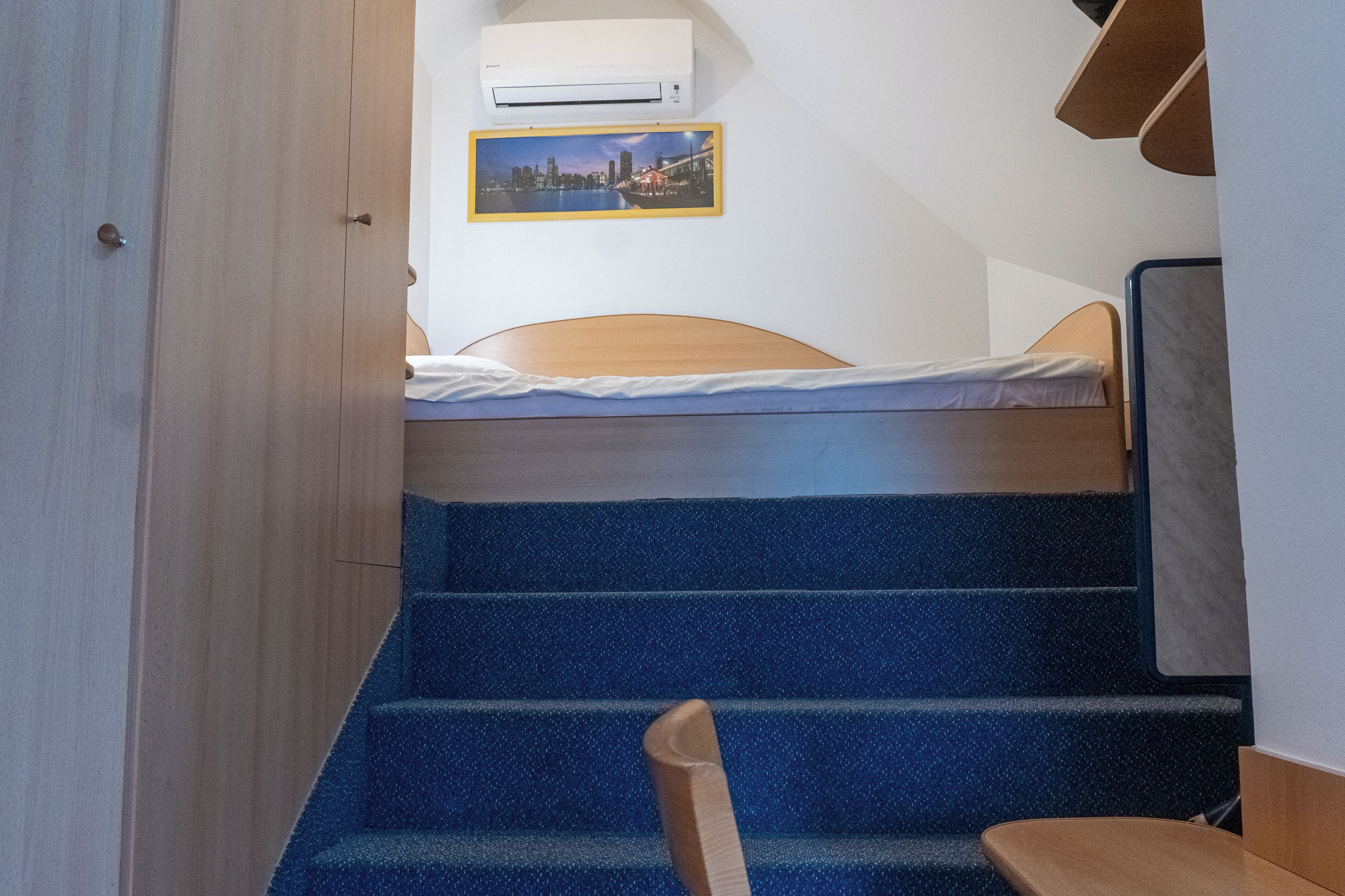 A bedroom with a bed, a window, a picture on the wall, and a staircase.
