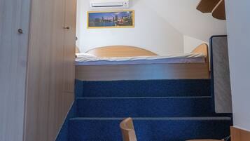 A bedroom with a bed, a window, a picture on the wall, and a staircase.