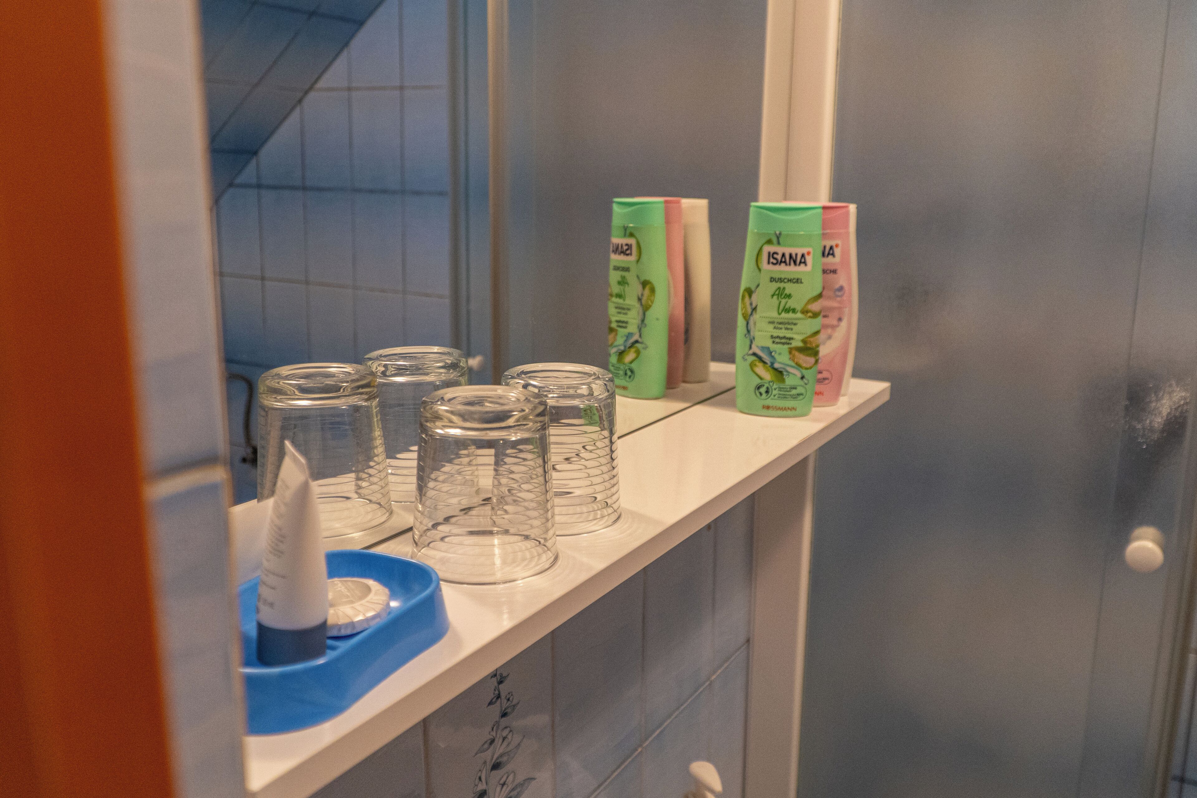 A bathroom shelf with clear glass jars, a blue dish, and two green and pink toiletry boxes.