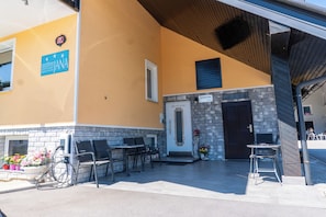 A hotel entrance with a reception desk, outdoor seating, and a sign for 'Sobe Rooms Zimmermann Apartments.' - Rooms & Apartments Jana (Cerklje na Gorenjskem)