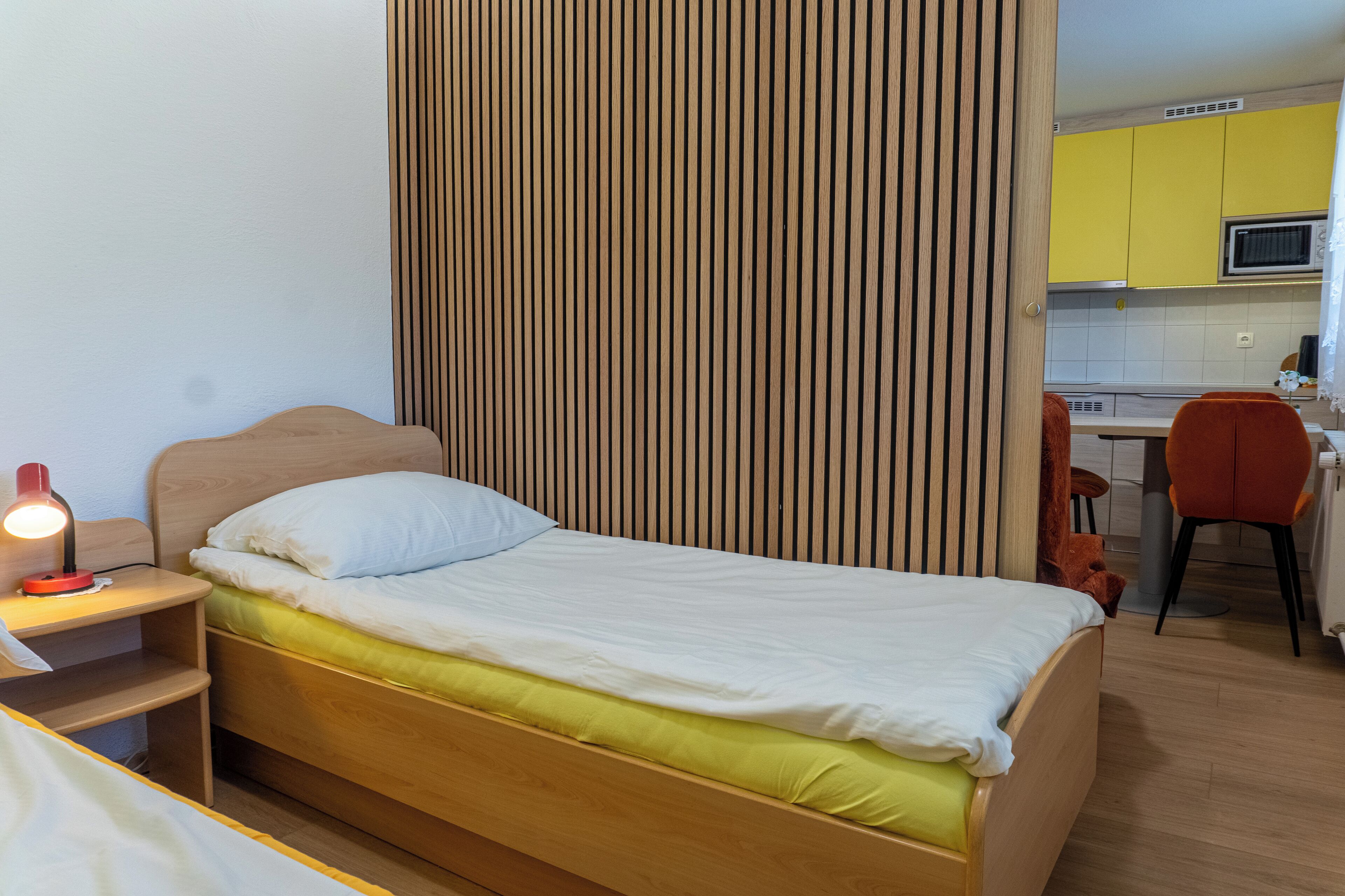 A room with a bed, a desk, a chair, and a kitchen area.