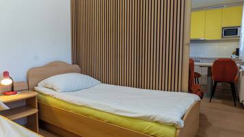 A room with a bed, a desk, a chair, and a kitchen area.