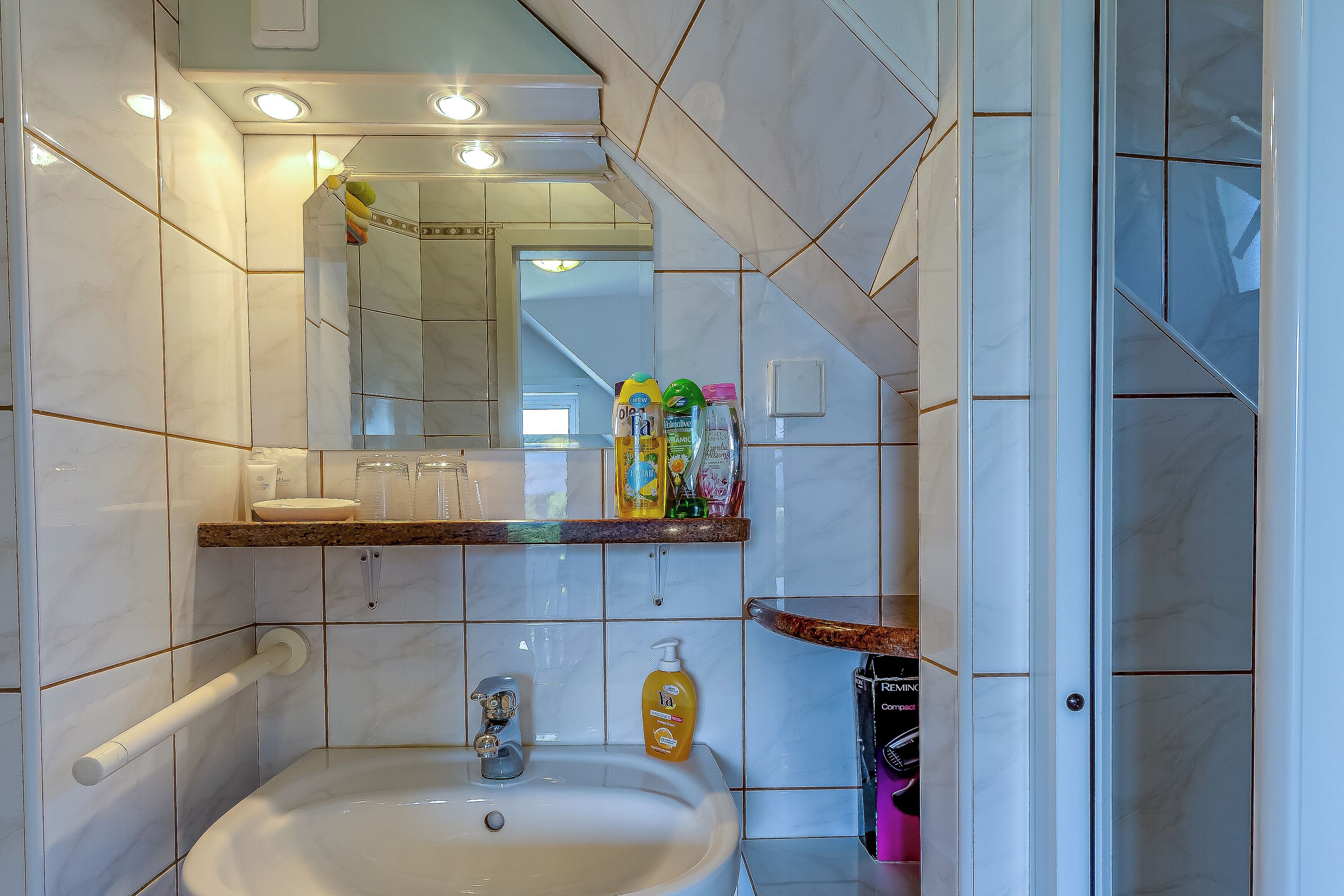 Ein Badezimmer mit Waschbecken, Spiegel und Pflegeprodukten auf einem Regal.
