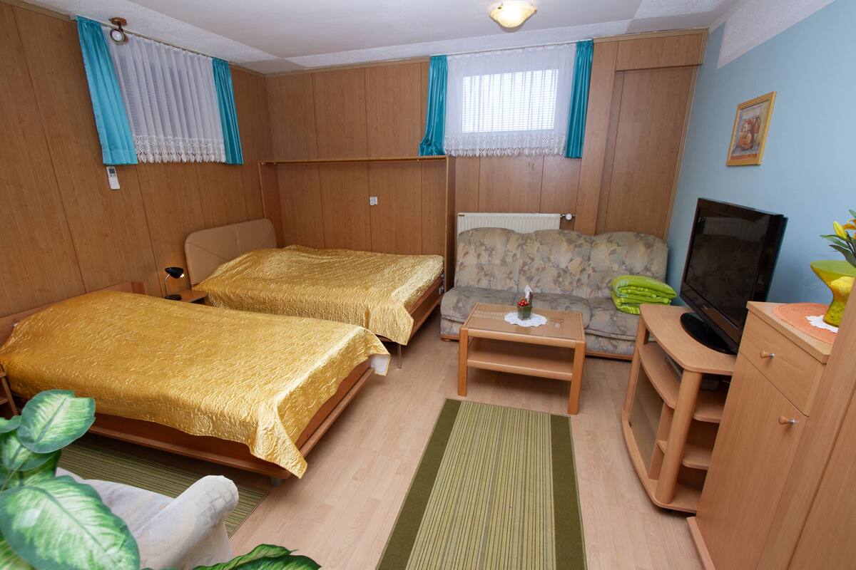 Ein Zimmer mit zwei Betten, einem Sofa, einem Fernseher und einem kleinen Tisch.
