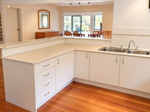 Une cuisine moderne avec des meubles blancs, un plan de travail en bois et une grande fenêtre qui laisse entrer la lumière naturelle.