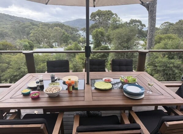 Une table à manger dressée avec des assiettes, des bols et des verres, donnant sur un paysage montagneux.