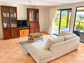 Een woonkamer met een bank, een televisie, een boekenkast en een balkon met uitzicht.