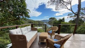 Eine Holzterrasse mit Korbmöbeln, darunter eine Couch und Stühle, mit Blick auf eine natürliche Landschaft.