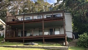 Ein zweistöckiges Gebäude mit Balkon, umgeben von viel Grün.
