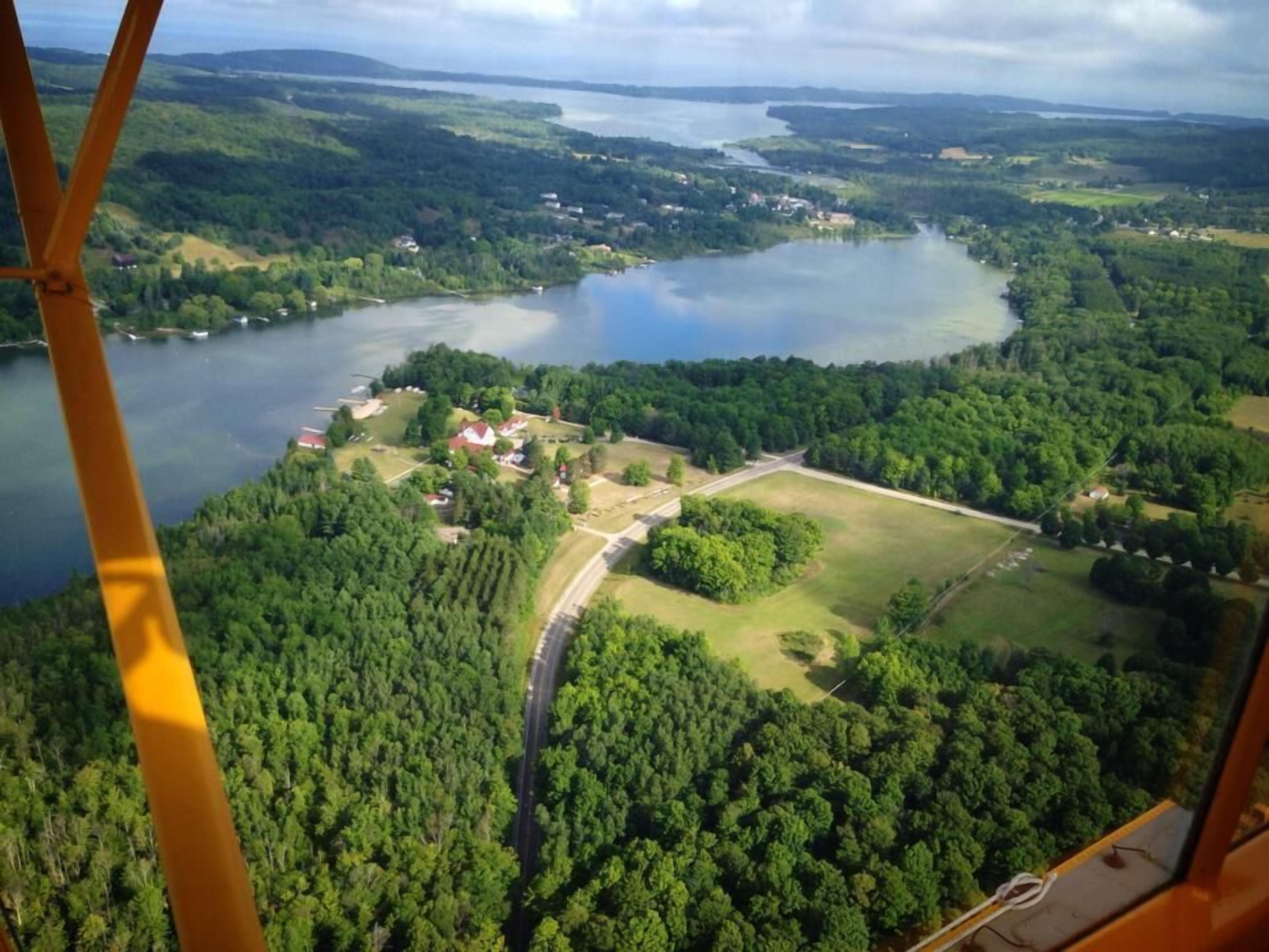 An aerial view of a lakeside area with a road, buildings, and dense forest.