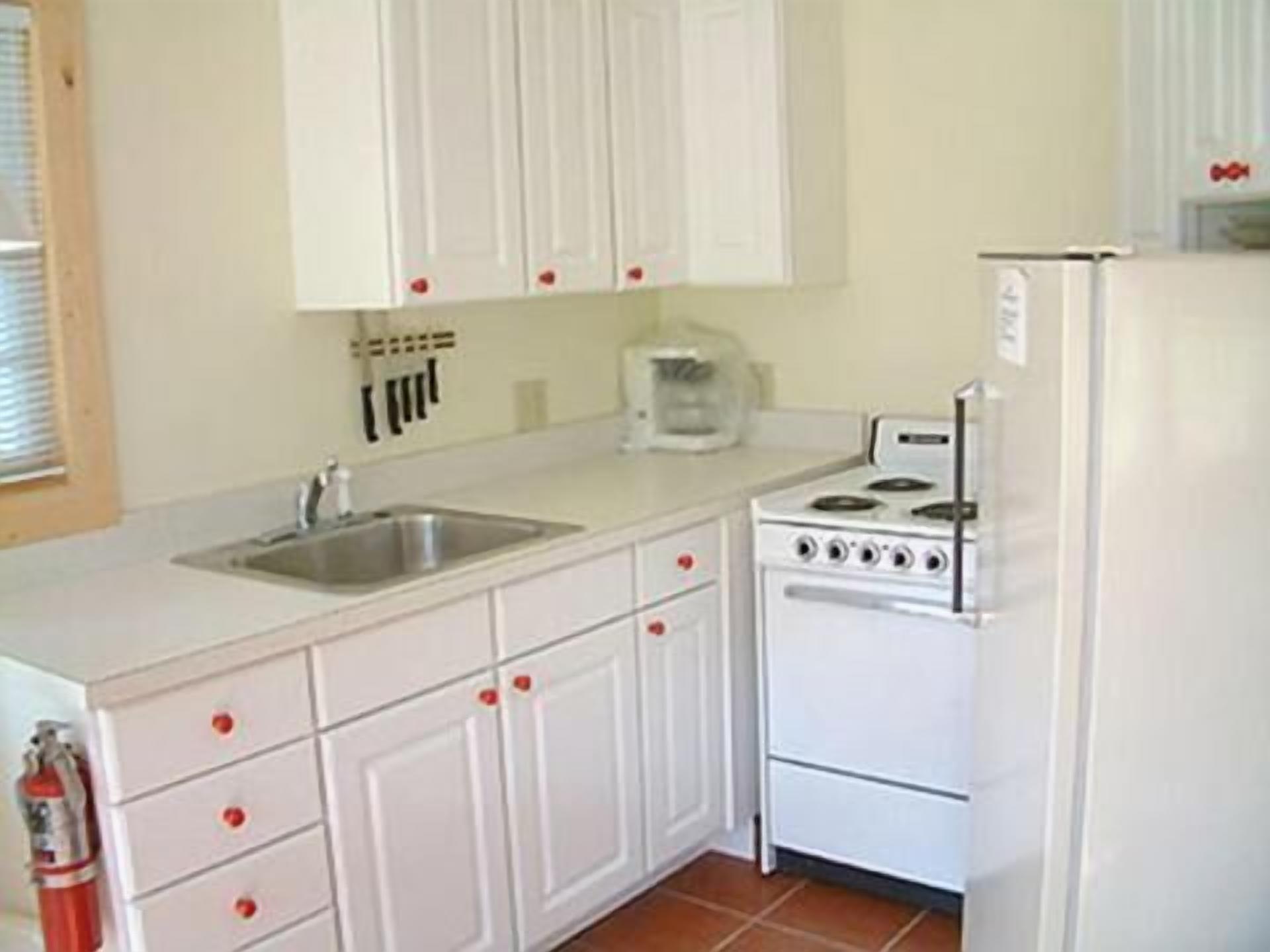 A kitchen with white cabinets, a stainless steel sink, and a white stove.