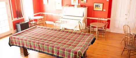 A room with a large bed, a piano, several chairs, and a dining table.