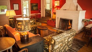 Ein gemütliches Wohnzimmer mit Kamin, Möbeln mit floralem Muster und einer Treppe, die in eine obere Etage führt.