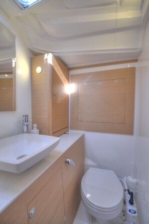 A modern bathroom with a wooden vanity, a white sink, and a toilet. - A Yacht In The City (Lagos)