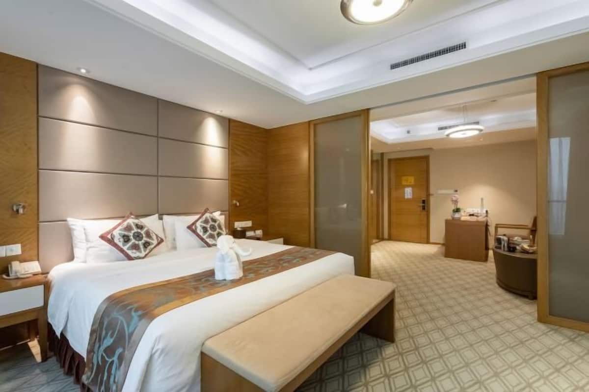 Ein Hotelzimmer mit einem großen Bett, Nachttischen, einer Bank, einem Schreibtisch und einem Spiegel.