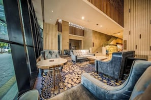 A modern lobby with seating arrangements, a patterned floor, and a staircase leading to an upper level.