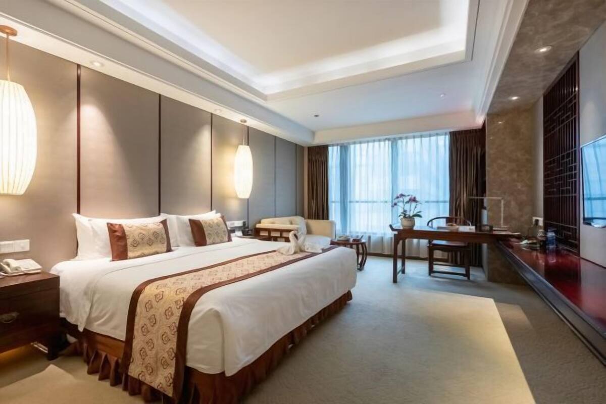 Ein Hotelzimmer mit einem großen Bett, einem Schreibtisch, einem Stuhl, einem Telefon und einem Vorhangfenster.