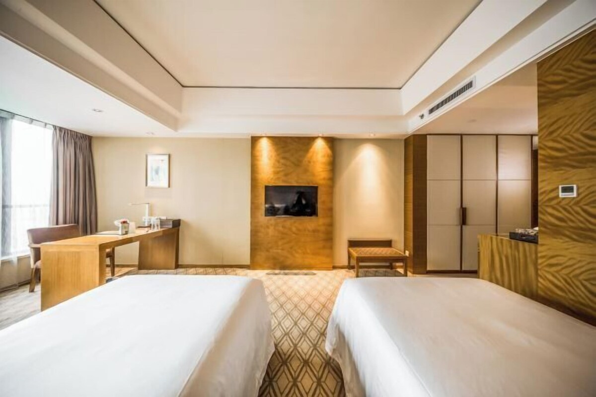 A hotel room with two beds, a desk, a chair, a TV, and a wardrobe.