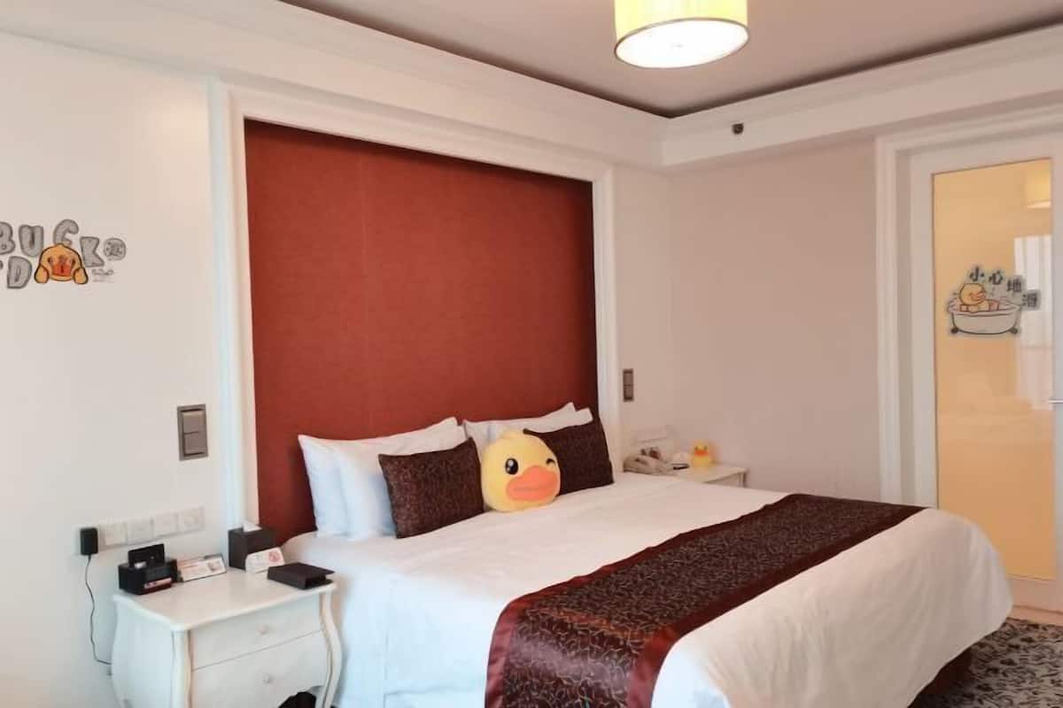 Ein Hotelzimmer mit einem großen Bett, einem Nachttisch, einem roten Kopfteil und einer Wand mit einem Enten-Sticker.