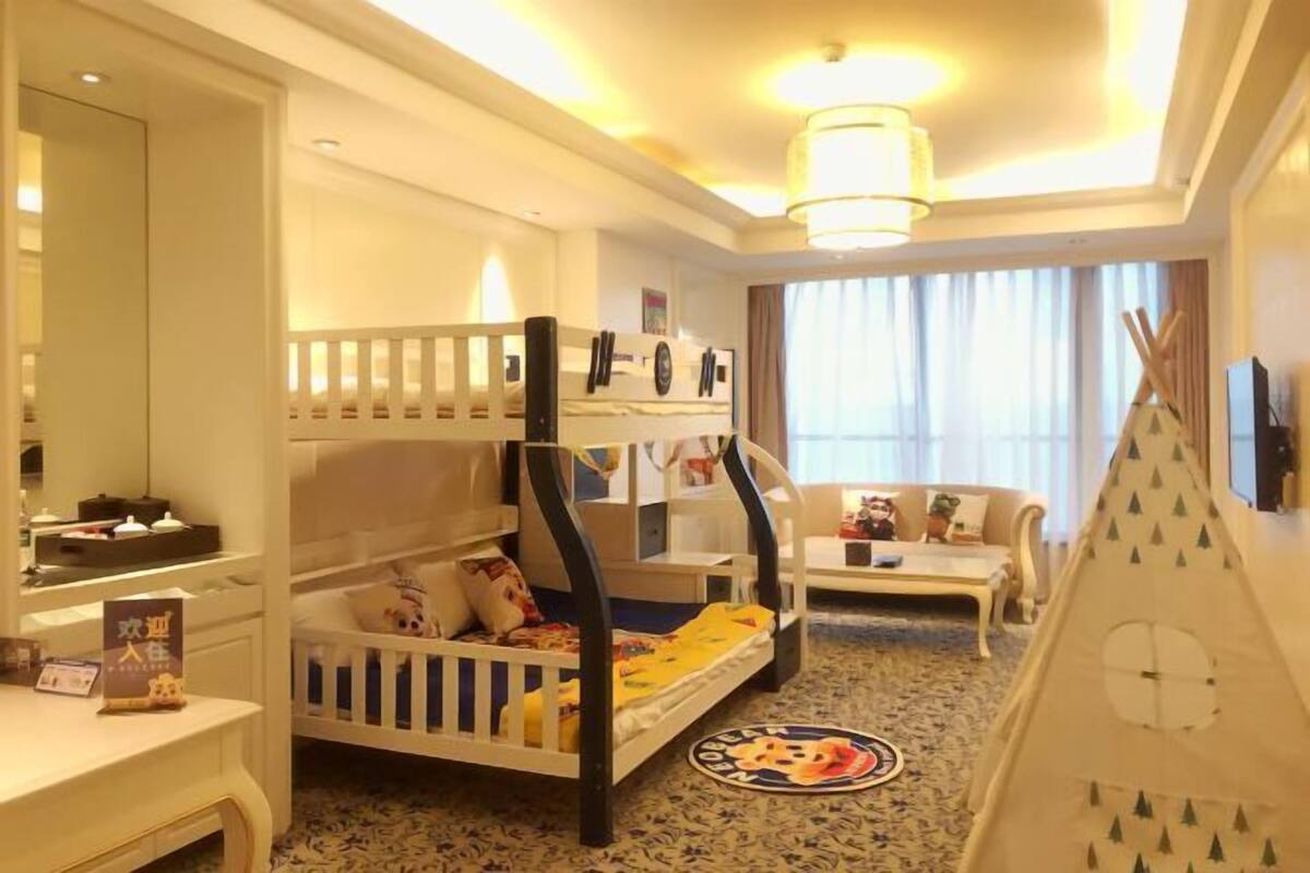 Ein familienfreundliches Hotelzimmer mit Stockbetten, einer Couch, einer zeltähnlichen Spielecke und einem runden Teppich mit einer Zeichentrickfigur.