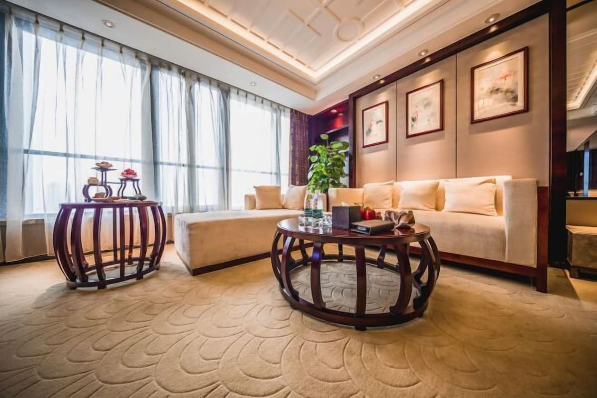 A modern living room with a beige sofa, two round wooden coffee tables, and a large window with sheer curtains.