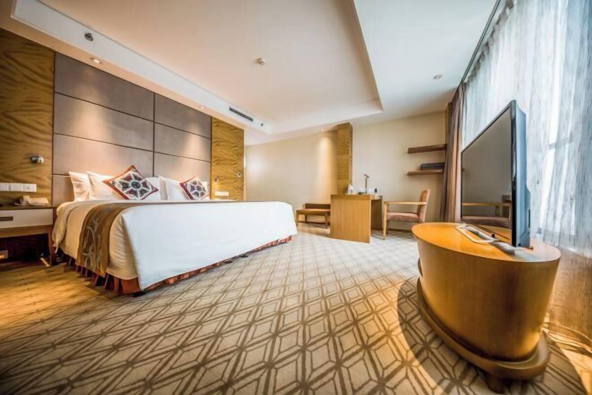 Ein modernes Hotelzimmer mit einem großen Bett, einem Holfnachtschränkchen, einem Schreibtisch und einem Fernseher.