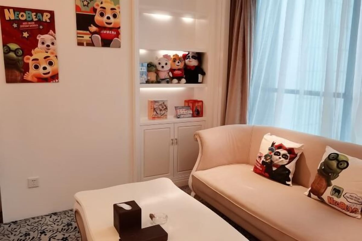 A room with a sofa, a small table, a cabinet, and wall decorations including plush toys and a poster.