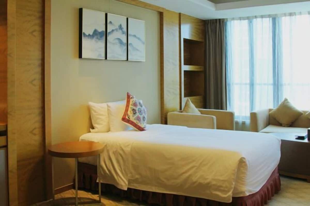 Ein Hotelzimmer mit einem Bett, einem kleinen runden Tisch, einer Couch und einem an der Wand befestigten Regal.
