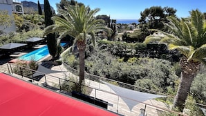 A pool area with a clear view of the sea, surrounded by palm trees and a red awning. - The Address Cassis (Cassis)