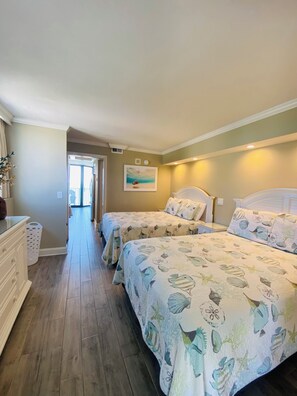 Habitación de hotel con dos camas, un pasillo que lleva a un balcón y un cuadro en la pared.