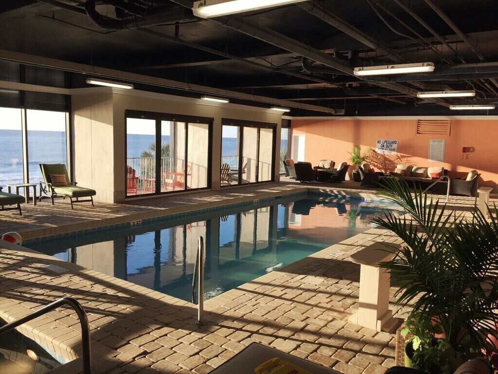 An indoor swimming pool with a view of the ocean, lounge chairs, and a 'No Lifeguard' sign.
