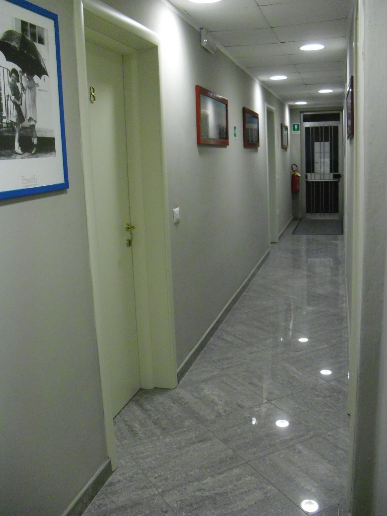 A hallway with a tiled floor, a framed picture on the wall, and a door with a number.
