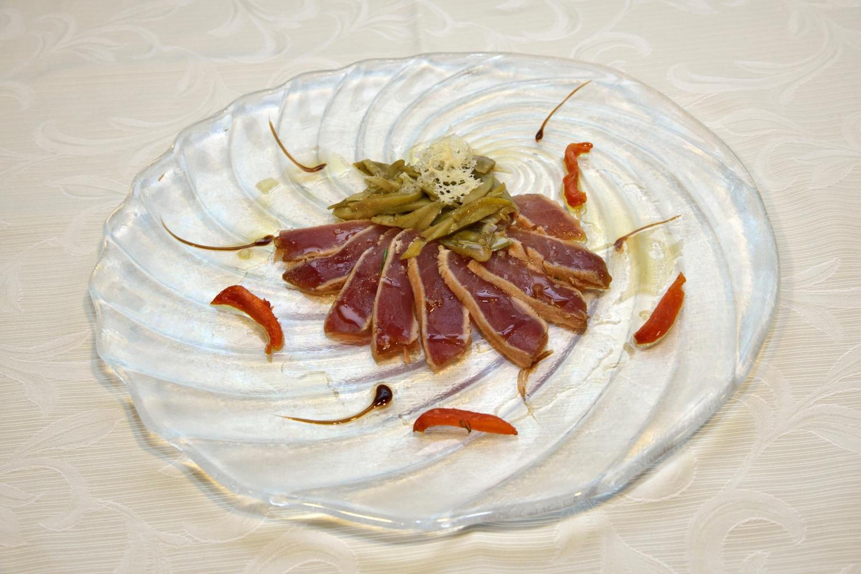 Un plato de vidrio con carne cortada, judías verdes y chiles rojos.
