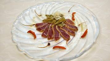 Un plato de vidrio con carne cortada, judías verdes y chiles rojos.