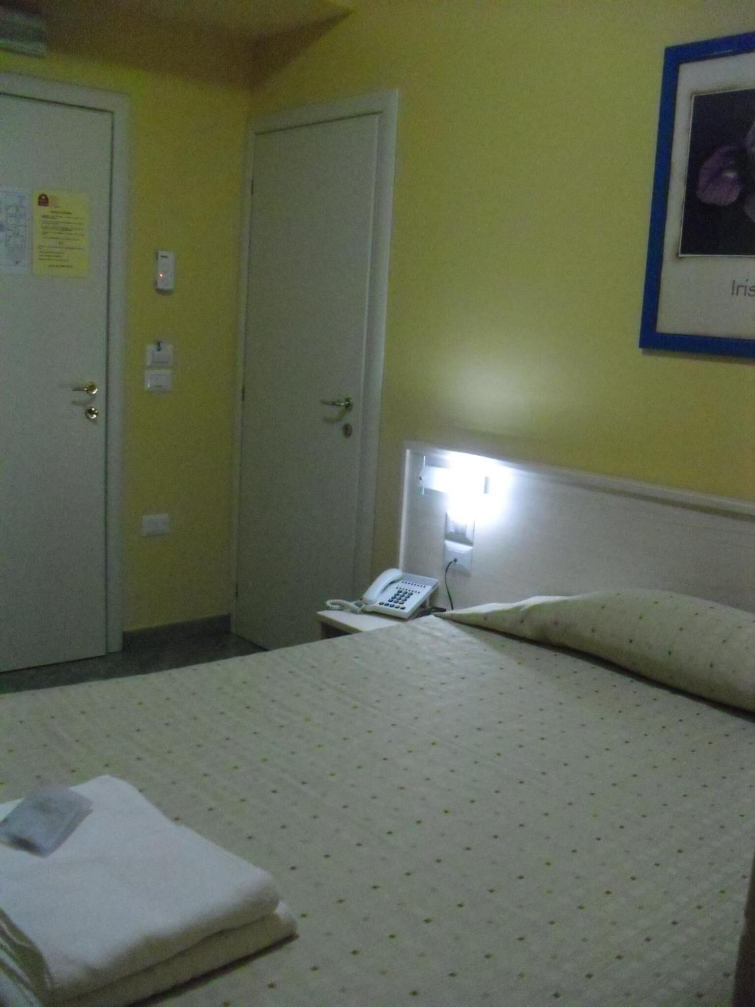 A hotel room with a bed, a bedside telephone, and a door with a light switch.