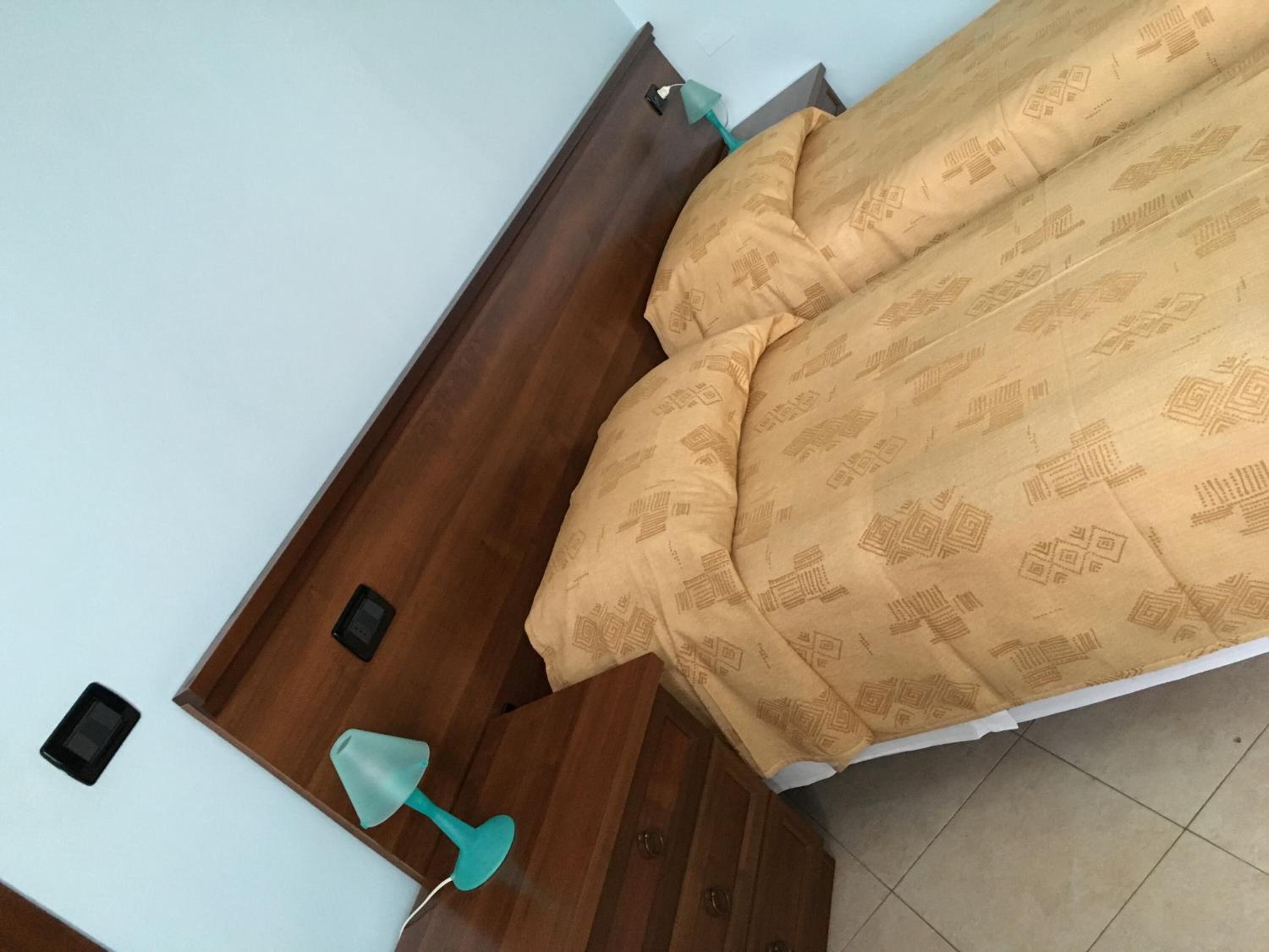Een slaapkamer met een houten hoofdbord, een bed met beddengoed met een patroon, een nachtkastje en een nachttafel.